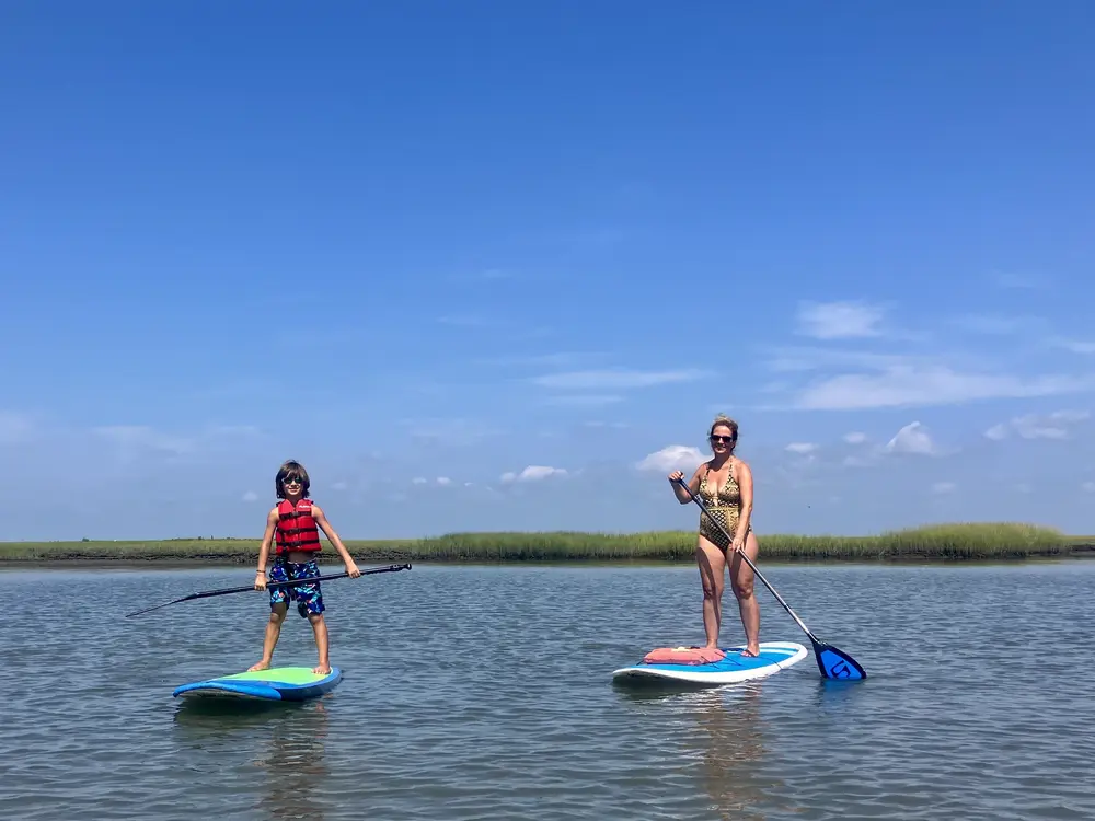 A mother and son enjoy a paddleboarding tour in Barnegat Bay, located on the Jersey Shore. They are both smiling at the camera