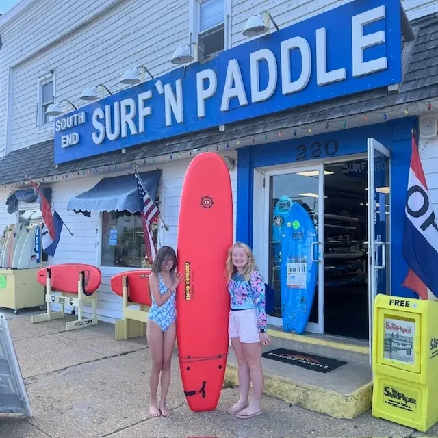 Two young children pose with surfboard rental outside South End Surf n’ Paddle’s Beach Haven surf shop