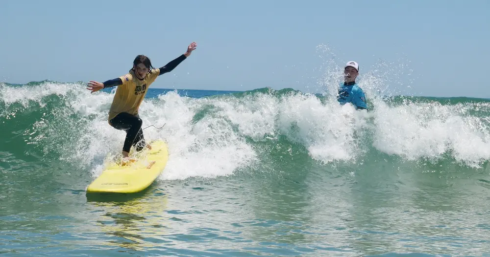 Teenager catches a wave during LBI surf lesson, their instructor observes from nearby