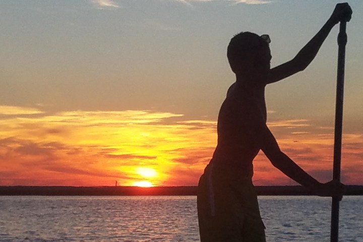 a man standing in front of a sunset over a body of water