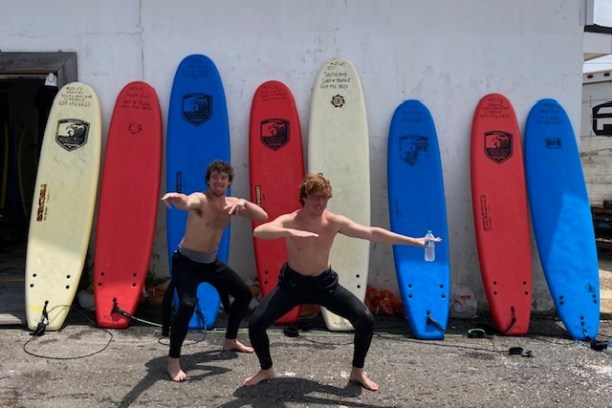 a group of people standing in front of a beach holding a surfboard